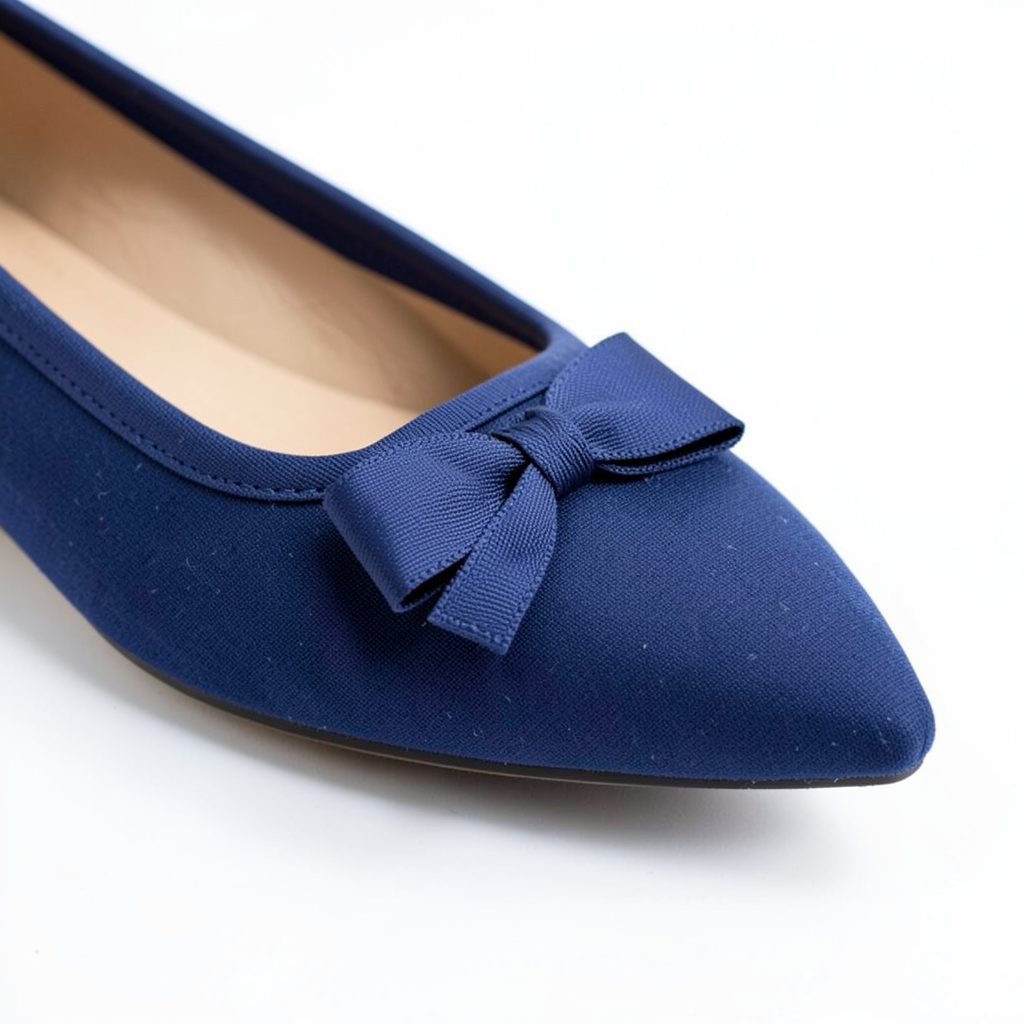 Close-up of a navy blue pointed-toe flat with a grosgrain bow on a clean white background