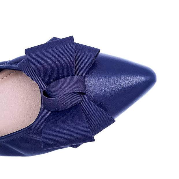 Close-up top view of a navy blue pointed-toe flat with a grosgrain bow on a white background