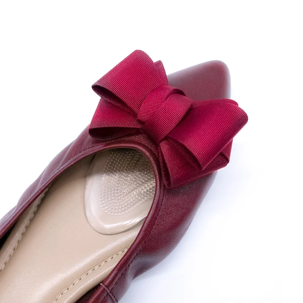 Close-up top view of a dark red pointed-toe flat with a grosgrain bow on a white background